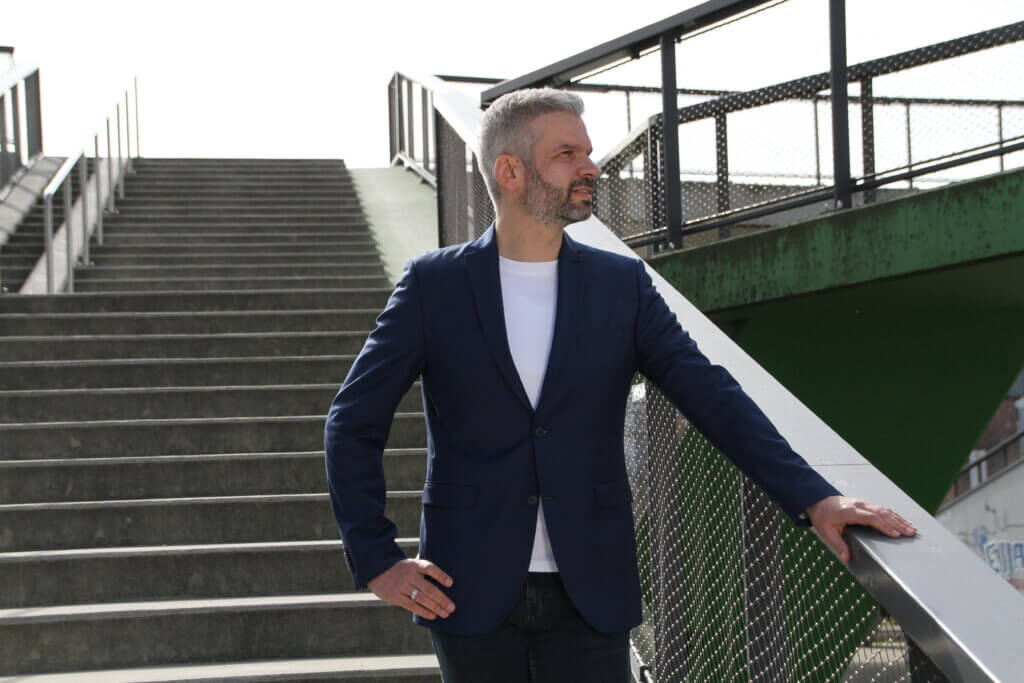 Eigenverantwortung Mitarbeiter abgeben – Business Coach steht an einer Außentreppe und blickt vorausschauend zur Seite